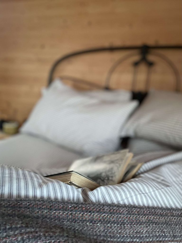 A daytime shot of the bed, the bedding is purposefully messy with an open book, suggesting a day spent relaxing in the stylish bedroom.