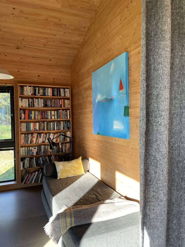 The reading nook chaise longue, with the bookcase behind, and an example of the stylish local artwork featured throughout The Black Shed.