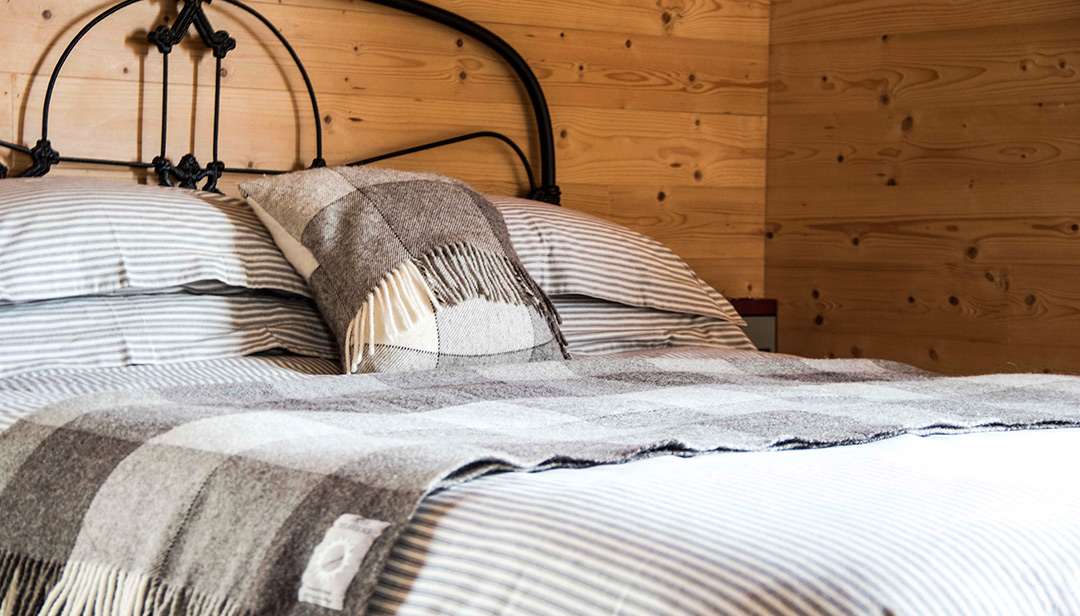 A wide angle shot of the made-up bed, with stylish Skye Weavers throws and soft furnishings. 